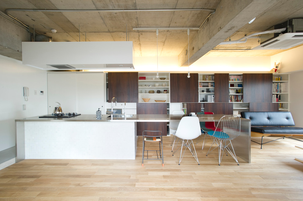 Foto på ett industriellt vit linjärt kök med öppen planlösning, med en halv köksö, bänkskiva i rostfritt stål, ljust trägolv, en integrerad diskho, skåp i mörkt trä, stänkskydd med metallisk yta, svarta vitvaror och beiget golv