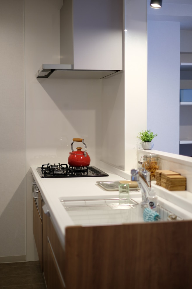 This is an example of a medium sized modern single-wall open plan kitchen in Other with a single-bowl sink, flat-panel cabinets, medium wood cabinets, composite countertops, brown splashback, glass sheet splashback, black appliances, plywood flooring, an island, brown floors and white worktops.