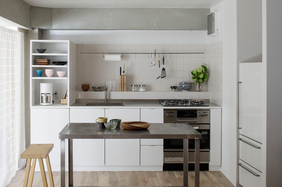 Inspiration for an industrial single-wall kitchen in Tokyo with a single-bowl sink, flat-panel cabinets, white cabinets, stainless steel worktops, white splashback, painted wood flooring and brown floors.