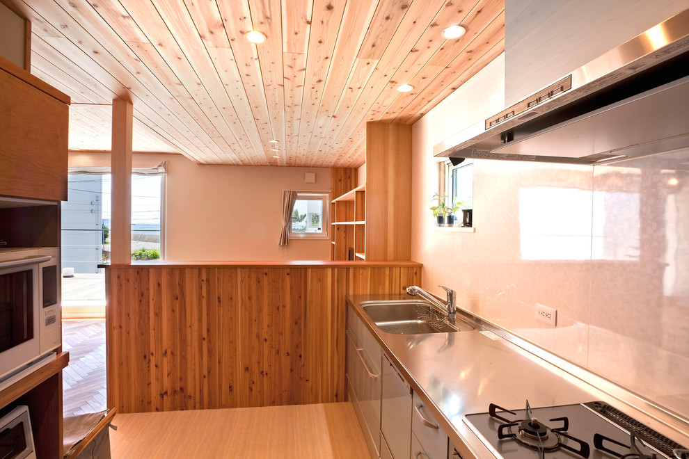 Immagine di un cucina con isola centrale stile rurale con top in acciaio inossidabile, paraspruzzi bianco e pavimento beige