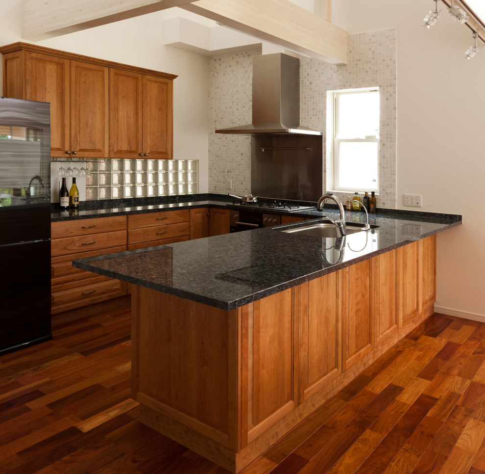 Example of a large arts and crafts u-shaped medium tone wood floor eat-in kitchen design in Tokyo with an undermount sink, raised-panel cabinets, light wood cabinets, green backsplash, mosaic tile backsplash, black appliances, no island and granite countertops