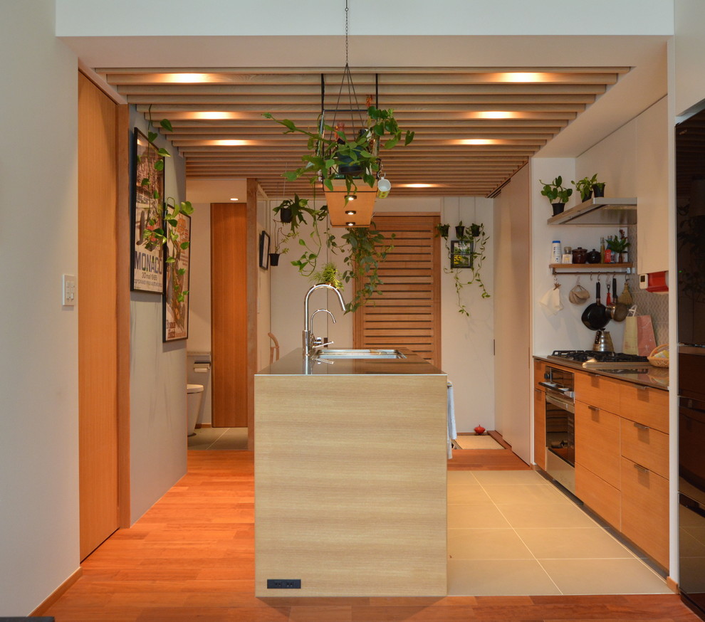 東京23区にある小さなコンテンポラリースタイルのおしゃれなキッチン (フラットパネル扉のキャビネット、淡色木目調キャビネット、ステンレスカウンター、木材のキッチンパネル、黒い調理設備、無垢フローリング、茶色い床) の写真