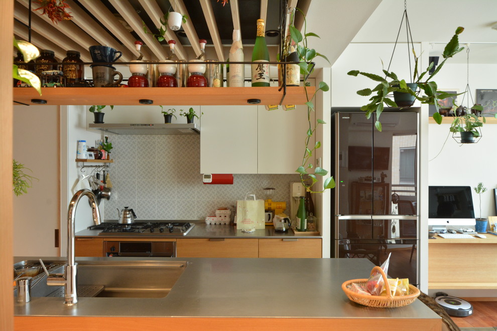 Zweizeilige, Kleine Moderne Wohnküche mit flächenbündigen Schrankfronten, hellen Holzschränken, Edelstahl-Arbeitsplatte, Rückwand aus Holz, schwarzen Elektrogeräten, braunem Holzboden, Kücheninsel und braunem Boden in Tokio