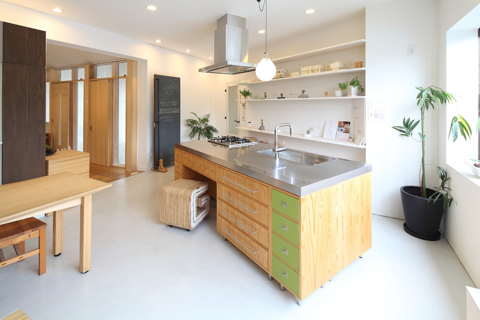 Minimalistisk inredning av ett kök, med en enkel diskho, släta luckor, gröna skåp, bänkskiva i rostfritt stål och en köksö
