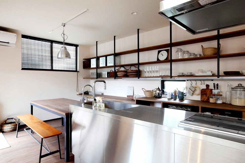 На фото: прямая кухня в стиле лофт с обеденным столом, одинарной мойкой, столешницей из нержавеющей стали, паркетным полом среднего тона, островом и коричневым полом