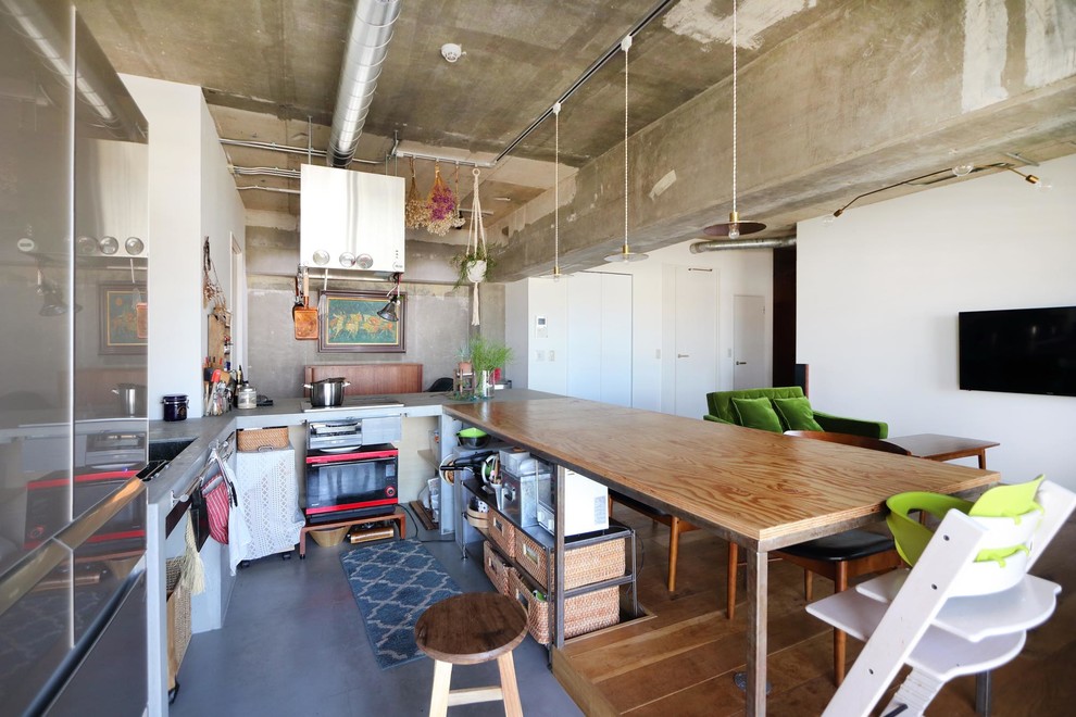 Inredning av ett rustikt l-kök, med en enkel diskho, öppna hyllor, bänkskiva i betong, betonggolv, en halv köksö och grått golv