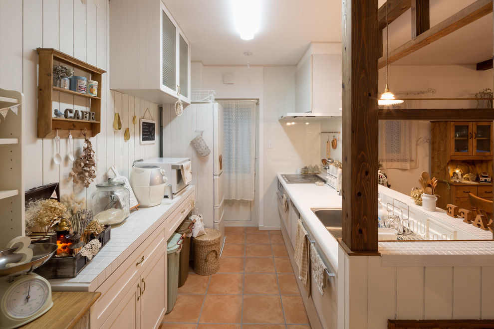This is an example of a country single-wall open plan kitchen in Other with composite countertops, white splashback, white appliances, terracotta flooring, orange floors, white worktops, a single-bowl sink, recessed-panel cabinets and a breakfast bar.