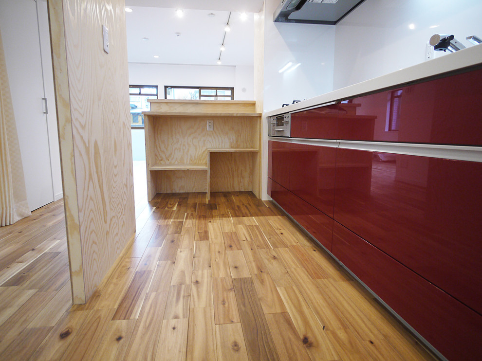 Cette image montre une cuisine linéaire chalet fermée avec des portes de placard rouges, un sol en bois brun, une crédence blanche et îlot.