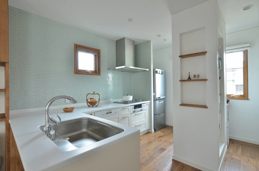 Exempel på ett minimalistiskt l-kök, med en enkel diskho, luckor med infälld panel, vita skåp, blått stänkskydd, mellanmörkt trägolv, en halv köksö och brunt golv