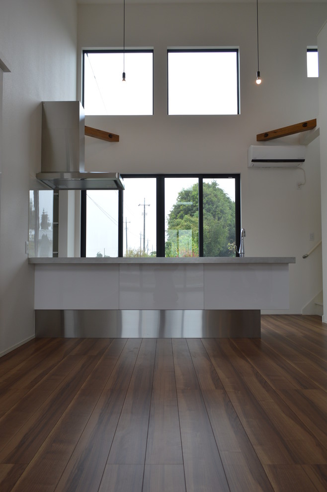 Пример оригинального дизайна: прямая кухня в стиле модернизм с обеденным столом, белыми фасадами, столешницей из нержавеющей стали, белым фартуком, черной техникой, полом из фанеры и полуостровом