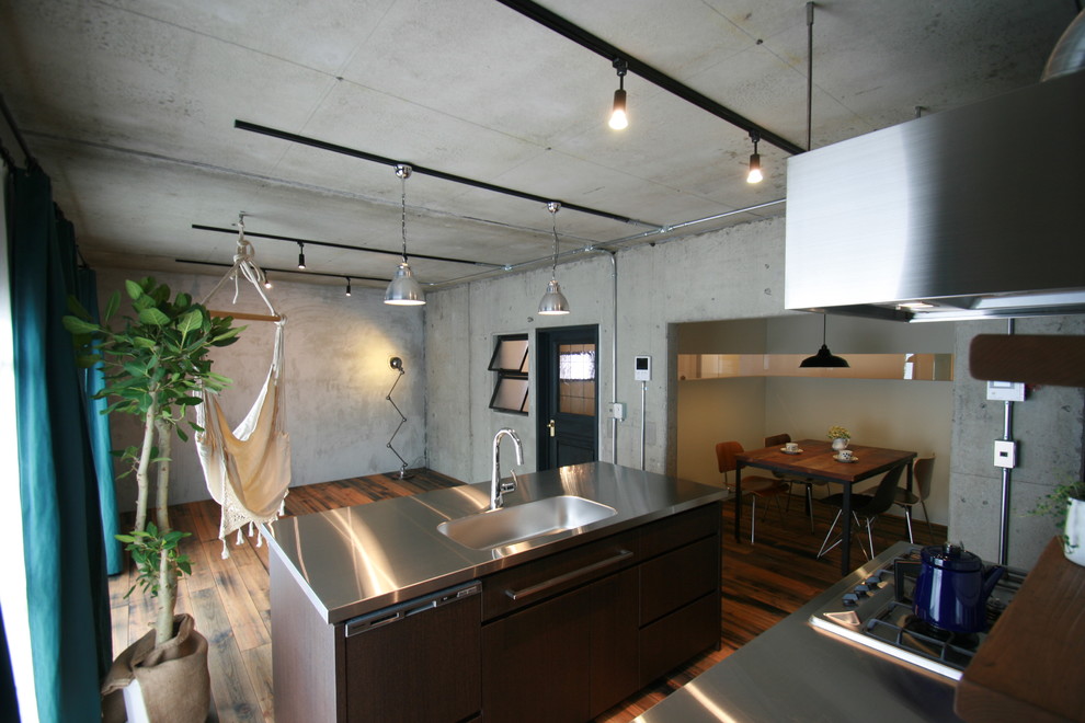 Foto di un cucina con isola centrale eclettico con lavello integrato, ante lisce, ante in legno bruno, top in acciaio inossidabile e pavimento in legno massello medio