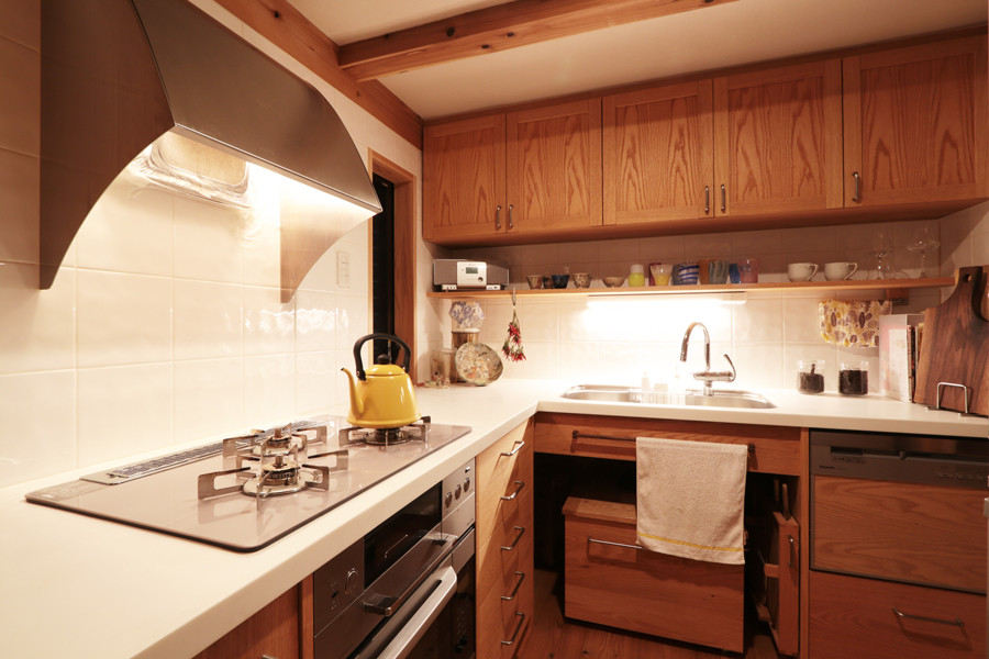 Cette photo montre une cuisine asiatique en L fermée avec un évier intégré, une crédence en céramique, un électroménager en acier inoxydable et un sol en bois brun.