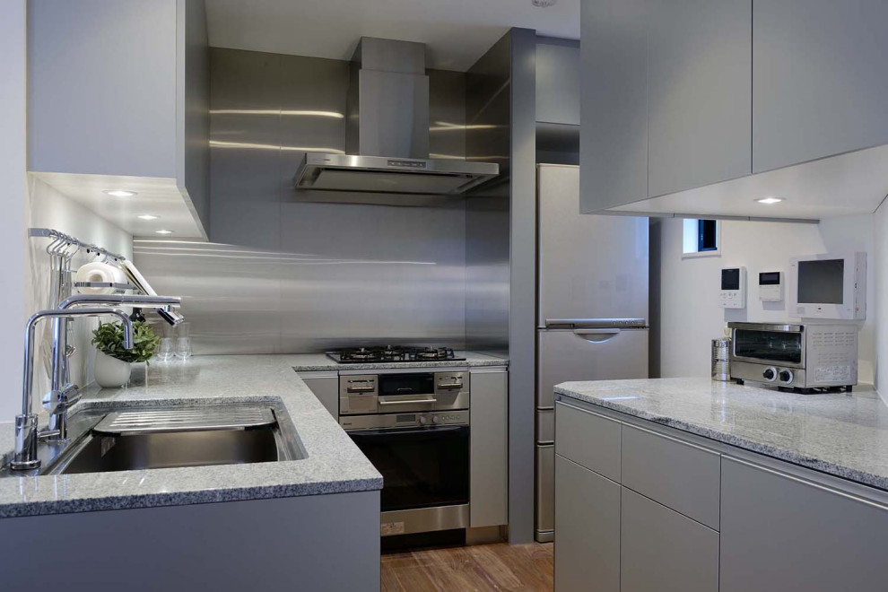Idéer för ett litet modernt grå kök, med en enkel diskho, släta luckor, grå skåp, granitbänkskiva, grått stänkskydd, stänkskydd i trä, rostfria vitvaror, plywoodgolv, en köksö och brunt golv