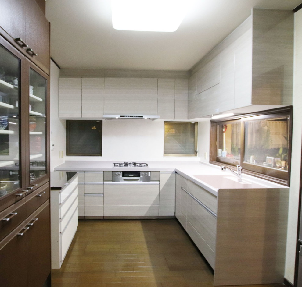 東京都下にある中くらいなモダンスタイルのおしゃれなキッチン (一体型シンク、インセット扉のキャビネット、淡色木目調キャビネット、人工大理石カウンター、白いキッチンパネル、シルバーの調理設備、茶色い床、白いキッチンカウンター) の写真