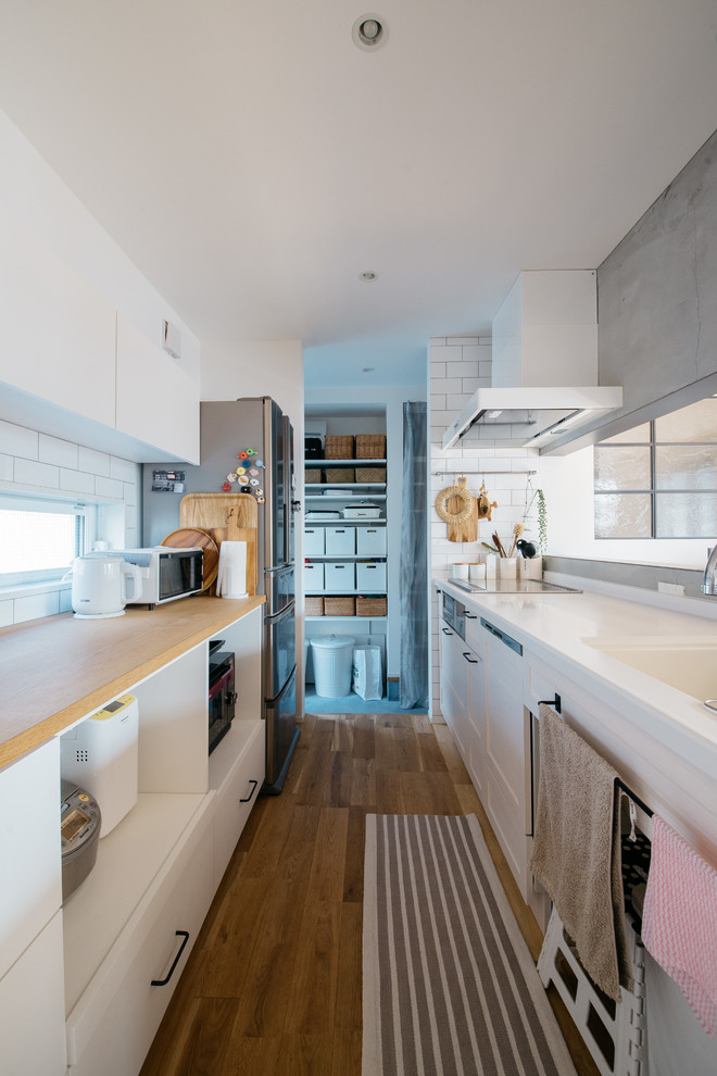 Inspiration pour une cuisine design avec des portes de placard blanches, un plan de travail en surface solide et un sol en bois brun.