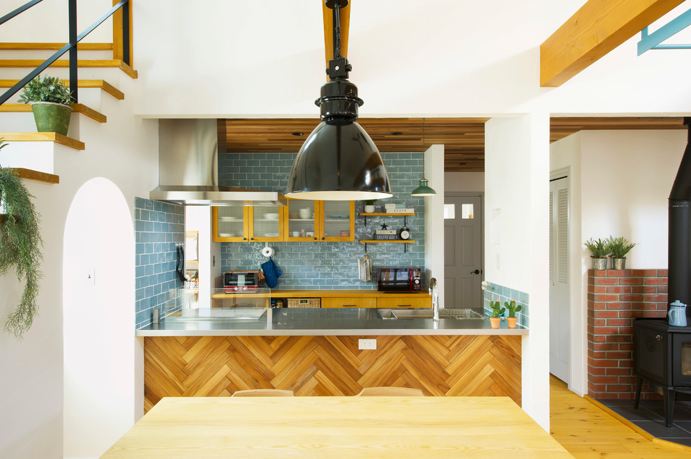 他の地域にある北欧スタイルのおしゃれなキッチン (一体型シンク、ガラス扉のキャビネット、淡色木目調キャビネット、ステンレスカウンター、青いキッチンパネル、サブウェイタイルのキッチンパネル、淡色無垢フローリング) の写真