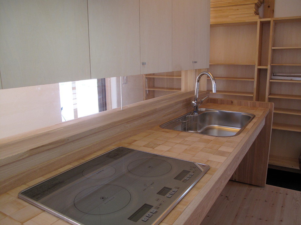 Modelo de cocina lineal asiática pequeña abierta con encimera de madera, electrodomésticos de acero inoxidable, suelo de madera clara, suelo beige y encimeras beige
