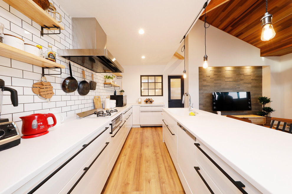 他の地域にあるインダストリアルスタイルのおしゃれなキッチン (一体型シンク、フラットパネル扉のキャビネット、白いキャビネット、白いキッチンパネル、無垢フローリング、茶色い床、白いキッチンカウンター) の写真