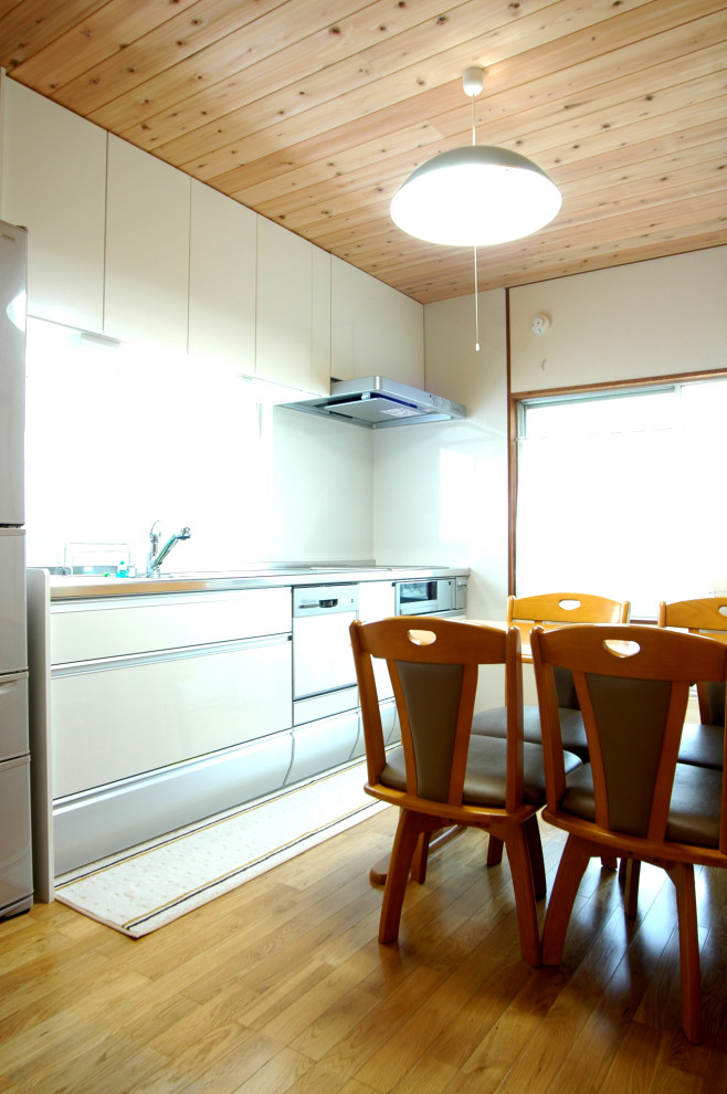 Exempel på ett mellanstort asiatiskt grå linjärt grått kök och matrum, med en enkel diskho, släta luckor, vita skåp, bänkskiva i rostfritt stål, vitt stänkskydd, rostfria vitvaror, mellanmörkt trägolv, en köksö och brunt golv