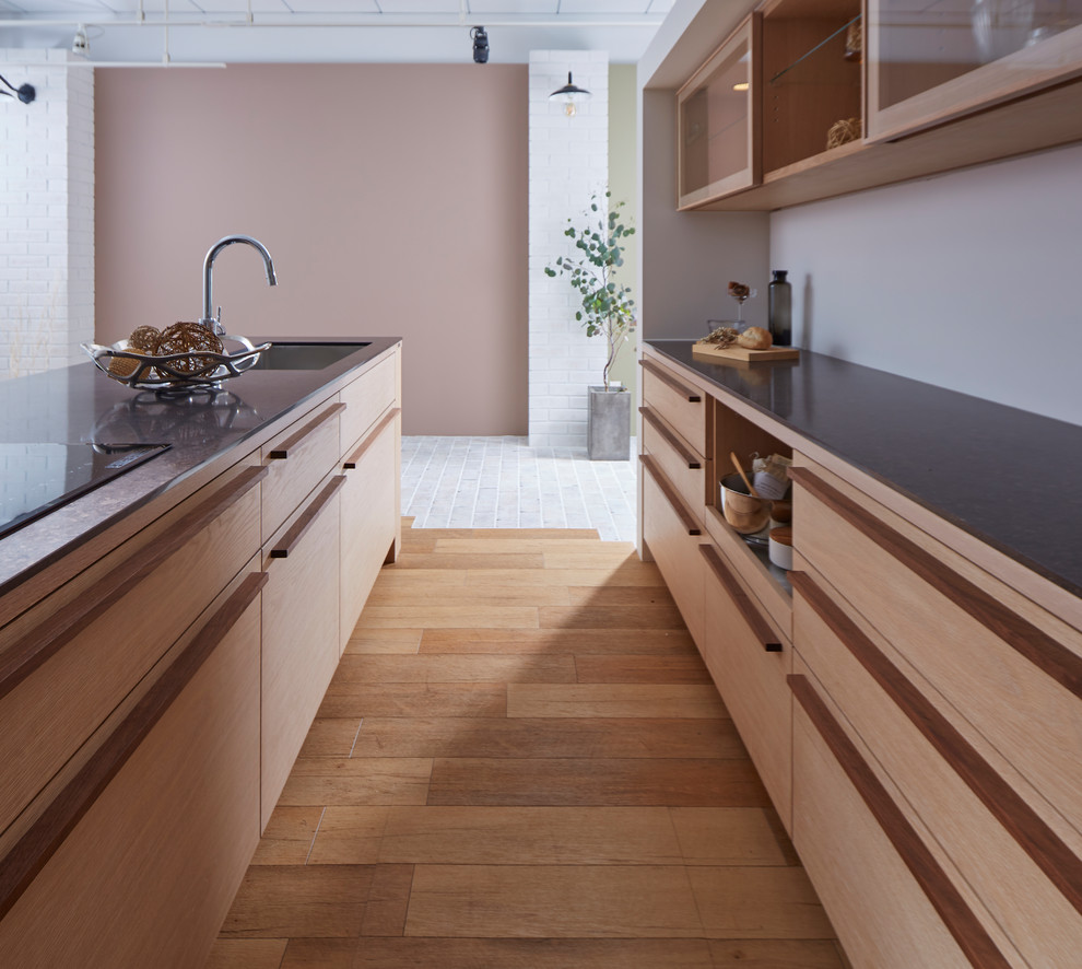 World-inspired kitchen in Other with a single-bowl sink, flat-panel cabinets, medium wood cabinets, medium hardwood flooring, an island and brown floors.