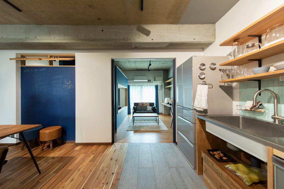 Diseño de cocina urbana con fregadero integrado, armarios abiertos, encimera de acero inoxidable, salpicadero gris y suelo de madera en tonos medios
