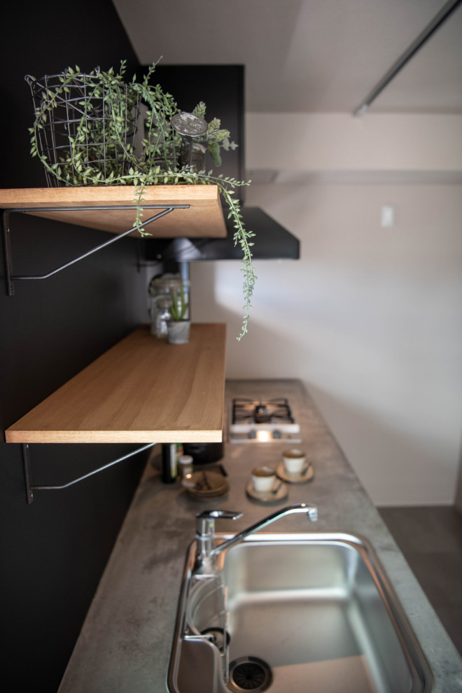 Idéer för ett avskilt, litet industriellt grå linjärt kök, med en nedsänkt diskho, öppna hyllor, skåp i ljust trä, bänkskiva i betong, svart stänkskydd och svarta vitvaror