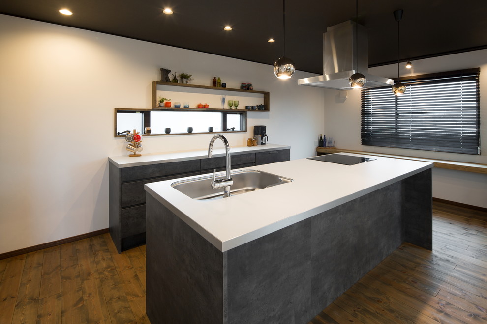 Cette photo montre une cuisine parallèle et grise et noire avec un évier 1 bac, un placard à porte plane, des portes de placard grises, un sol en bois brun et îlot.