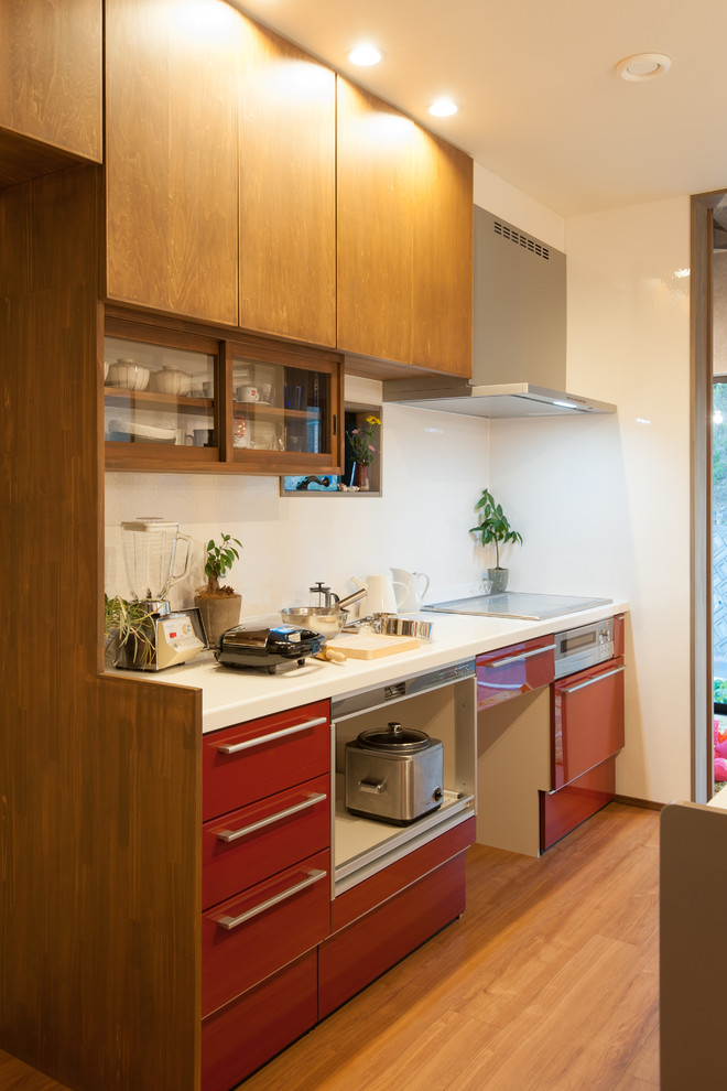 На фото: маленькая прямая кухня в восточном стиле с плоскими фасадами, красными фасадами, цветной техникой и паркетным полом среднего тона для на участке и в саду с