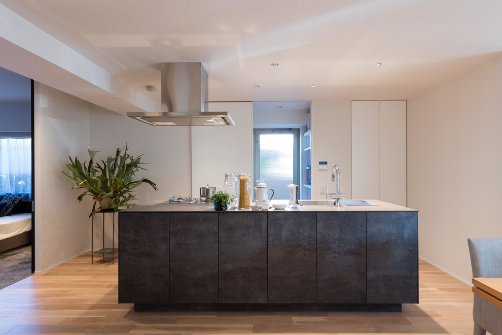 Immagine di una cucina minimalista con lavello a vasca singola, ante lisce, ante in legno bruno, top in acciaio inossidabile, parquet chiaro e pavimento marrone