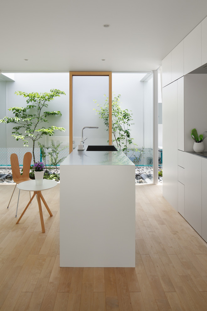 Imagen de cocina actual con fregadero integrado, armarios con paneles lisos, puertas de armario blancas, suelo de madera clara y una isla