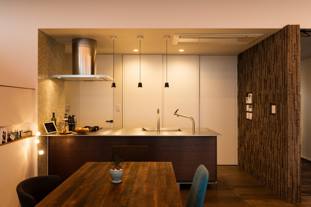 Cette image montre une cuisine ouverte design avec un évier 1 bac, un plan de travail en inox, un sol en bois brun, un sol marron et une péninsule.