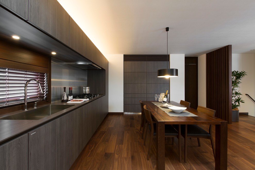Exempel på ett modernt linjärt kök med öppen planlösning, med släta luckor, skåp i mörkt trä, stänkskydd med metallisk yta, mörkt trägolv och en enkel diskho