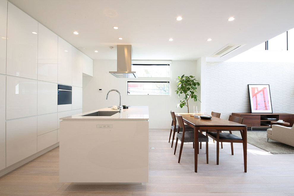 Foto di un cucina con isola centrale design con lavello sottopiano, ante lisce, ante bianche, elettrodomestici neri e parquet chiaro