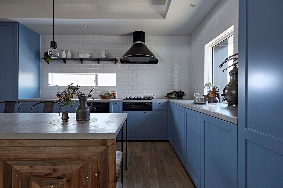 Diseño de cocina nórdica con puertas de armario azules, encimeras grises, armarios con paneles empotrados, salpicadero blanco, suelo de madera pintada, península y suelo gris