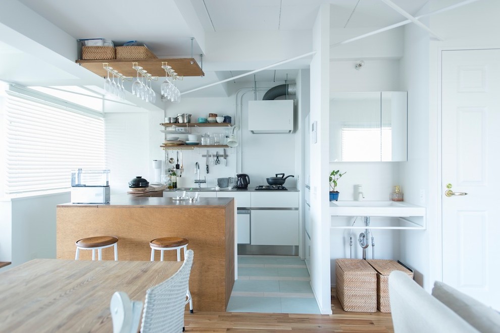 Photo of a small beach style single-wall open plan kitchen in Tokyo with a single-bowl sink, flat-panel cabinets, white cabinets, white splashback, an island, multi-coloured floors and brown worktops.