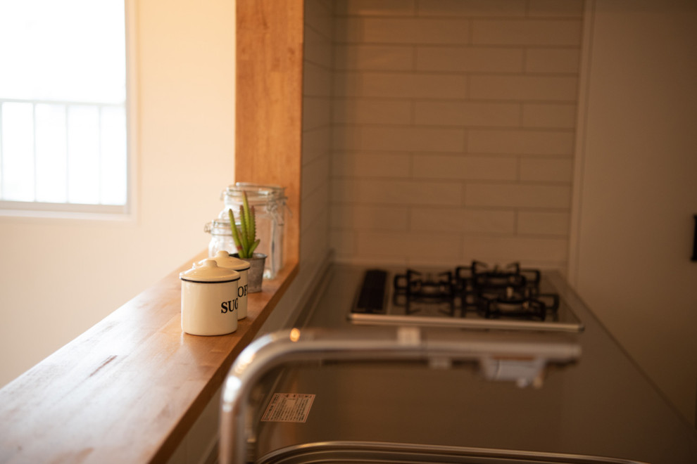 Exemple d'une cuisine ouverte linéaire industrielle avec un évier 1 bac, un placard à porte affleurante, un plan de travail en inox, une crédence blanche, une crédence en carreau briquette et un électroménager en acier inoxydable.