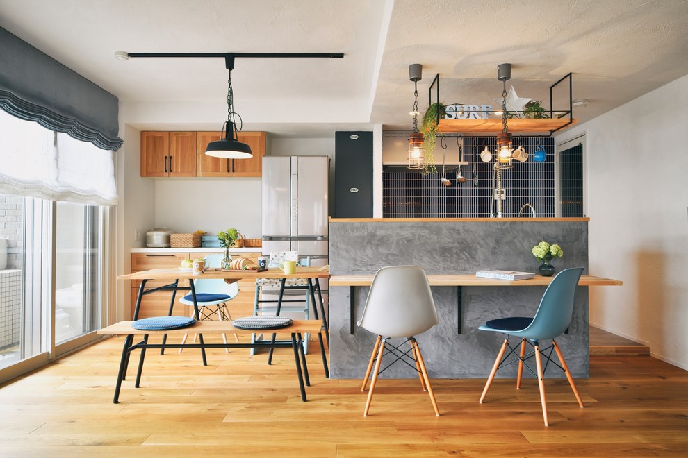 Photo of a world-inspired galley kitchen/diner in Other with shaker cabinets, medium wood cabinets, black splashback, white appliances, medium hardwood flooring, an island, brown floors and white worktops.