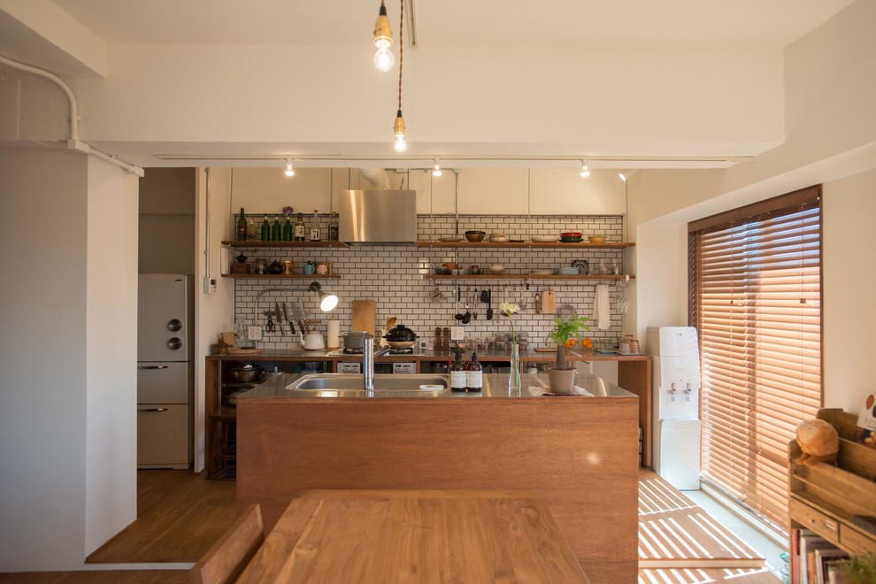 Zweizeilige Stilmix Wohnküche mit Edelstahl-Arbeitsplatte, Küchenrückwand in Weiß, Rückwand aus Metrofliesen, Kücheninsel, offenen Schränken, hellbraunen Holzschränken und braunem Holzboden in Tokio