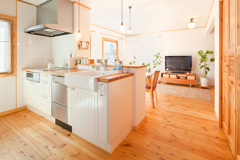 他の地域にある中くらいな北欧スタイルのおしゃれなキッチン (ドロップインシンク、落し込みパネル扉のキャビネット、白いキャビネット、木材カウンター、白いキッチンパネル、セラミックタイルのキッチンパネル、シルバーの調理設備、無垢フローリング、アイランドなし、茶色い床、茶色いキッチンカウンター) の写真