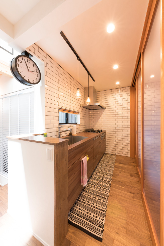 名古屋にある北欧スタイルのおしゃれなキッチン (シングルシンク、フラットパネル扉のキャビネット、中間色木目調キャビネット、木材カウンター、白いキッチンパネル、無垢フローリング、茶色い床) の写真