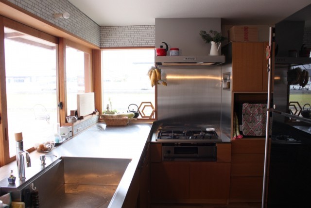 Imagen de cocinas en L abierta con encimera de acero inoxidable, fregadero integrado y puertas de armario de madera oscura