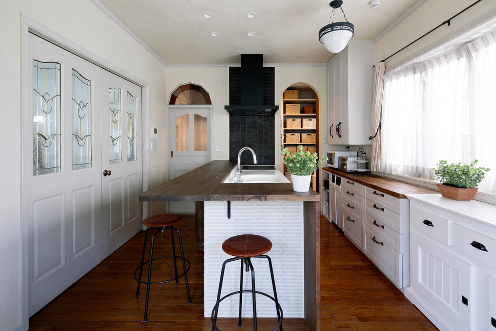 Idéer för vintage linjära kök, med en enkel diskho, luckor med infälld panel, vita skåp, mellanmörkt trägolv, en halv köksö och brunt golv