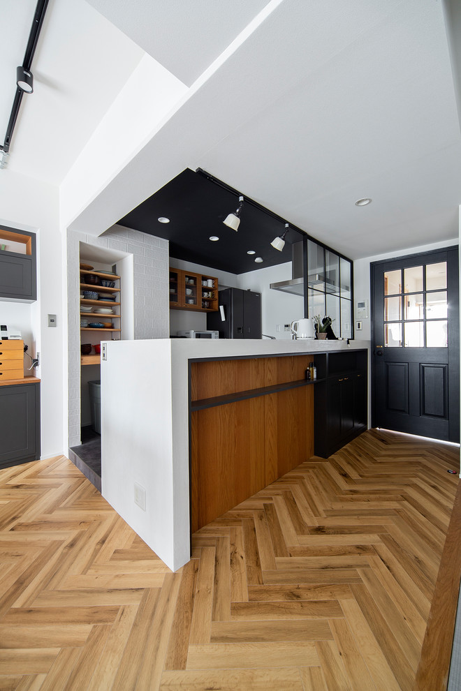This is an example of a contemporary galley kitchen in Osaka with concrete worktops, white splashback, black appliances, glass-front cabinets, medium wood cabinets, medium hardwood flooring, a breakfast bar, brown floors and white worktops.