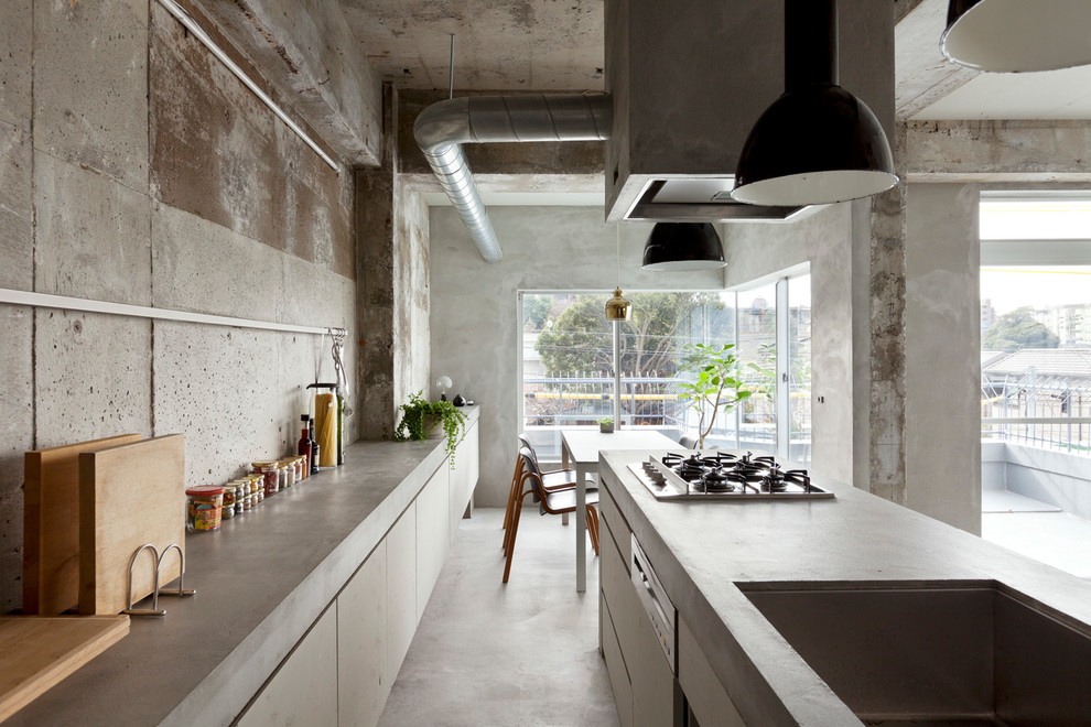 Industriell inredning av ett grå linjärt grått kök med öppen planlösning, med en enkel diskho, släta luckor, vita skåp, bänkskiva i betong, betonggolv och grått golv