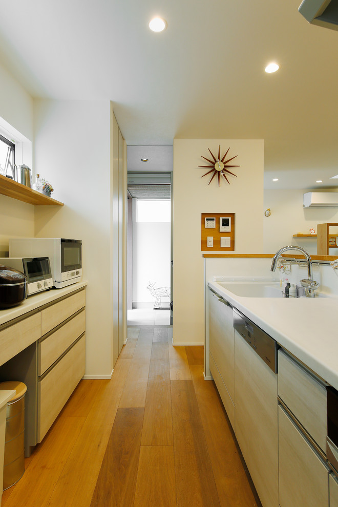 東京23区にあるお手頃価格の中くらいな北欧スタイルのおしゃれなキッチン (一体型シンク、フラットパネル扉のキャビネット、淡色木目調キャビネット、人工大理石カウンター、白いキッチンパネル、セラミックタイルのキッチンパネル、白い調理設備、無垢フローリング、茶色い床、白いキッチンカウンター) の写真