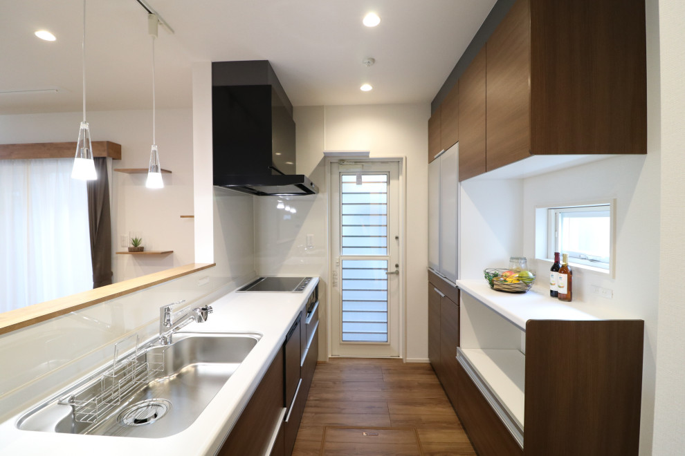 This is an example of a medium sized modern galley open plan kitchen in Other with a submerged sink, flat-panel cabinets, dark wood cabinets, composite countertops, white splashback, black appliances, plywood flooring, brown floors and white worktops.