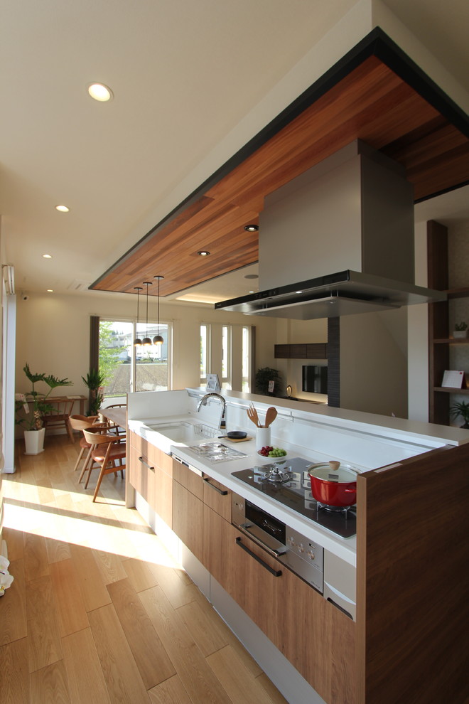 Large rustic single-wall open plan kitchen in Other with an integrated sink, medium wood cabinets, composite countertops, white appliances, light hardwood flooring, an island, brown floors, white worktops, flat-panel cabinets and white splashback.