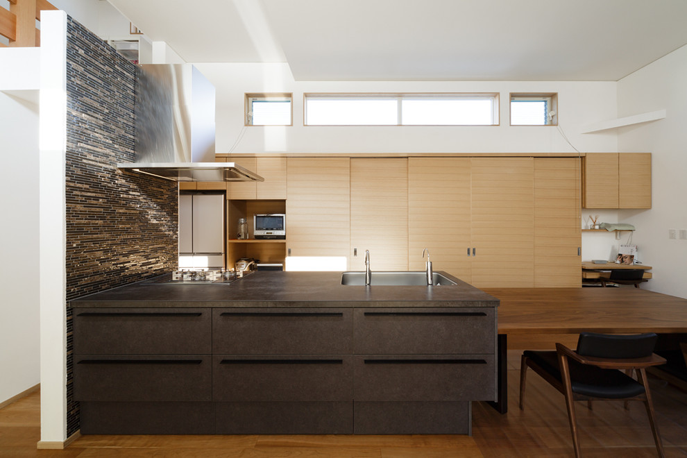 Cette photo montre une cuisine ouverte linéaire moderne avec un évier 1 bac, un placard à porte plane, des portes de placard marrons, un sol en bois brun, une péninsule, un sol marron et un plan de travail marron.