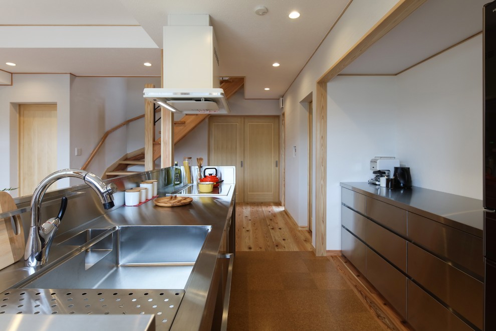 Example of a minimalist brown floor open concept kitchen design in Other with an integrated sink, flat-panel cabinets, stainless steel cabinets, stainless steel countertops, metallic backsplash and a peninsula