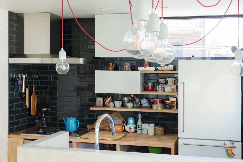 Photo of a small eclectic galley kitchen/diner in Tokyo with a submerged sink, white cabinets, wood worktops, ceramic splashback, coloured appliances, light hardwood flooring, beige floors, beige worktops and black splashback.
